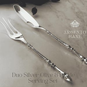Può includere: Un set da portata per olive e sottaceti in argento. Il set include una forchetta e un coltello con manici attorcigliati ed estremità decorative. Il testo "Duo Silver Olive & Pickle Serving Set" è in basso nell'immagine.