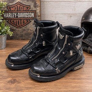 Peut inclure: Une paire de bottes en cuir noir avec une fermeture éclair frontale, des détails en métal argenté et la marque Harley-Davidson sur le côté et le bout. Les bottes présentent un col rembourré, une semelle en caoutchouc et des œillets métalliques.