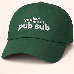 Puede incluir: Gorra de béisbol verde oscuro con la frase "you had me at pub sub" bordada en blanco. La gorra tiene una visera curva y un botón en la parte superior.