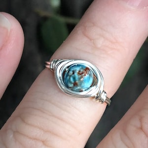 May include: A silver wire wrapped ring with a blue and brown gemstone.