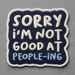 Puede incluir: Parche bordado con el texto "SORRY I'M NOT GOOD AT PEOPLE-ING" en hilo blanco roto y azul claro. El parche tiene un fondo azul marino con un borde blanco y es rectangular con bordes redondeados.