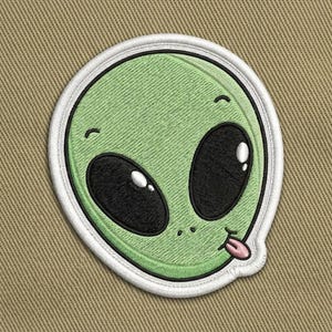 May include: Embroidered patch featuring a green alien face with large black eyes, a small pink tongue, and a white border. The alien has a friendly expression. The patch is on a tan background.