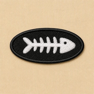 May include: An embroidered patch featuring a white fish skeleton design on a black oval background. The patch is set against a tan fabric, creating a contrast that highlights the detailed stitching of the fish bones.