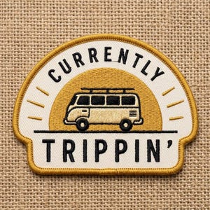 May include: Embroidered patch with a cream-colored background and a yellow border. The patch features a yellow sunburst design behind a beige van. The text "CURRENTLY TRIPPIN'" is displayed in black.