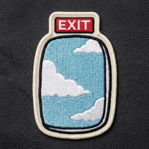 May include: Embroidered patch featuring a sky blue window with white clouds. The patch has a cream-colored border and a black outline. The word "EXIT" is displayed in red letters at the top of the patch.