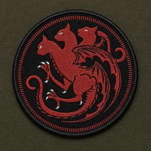 May include: A circular embroidered patch featuring a red three-headed cat creature with wings and a long tail on a black background. The design is enclosed by a thick black border with red stitching, showcasing detailed thread work and sharp claws.