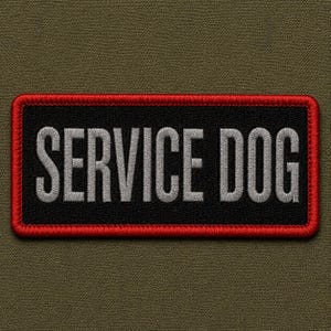 May include: A rectangular embroidered patch with a black background and a thick red border. The text SERVICE DOG is stitched in large, light gray capital letters across the center of the patch. The patch has a textured, fabric-like appearance.