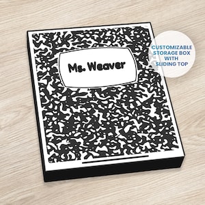 May include: A black and white composition notebook-style storage box with a sliding top. The box features a white label with the text "Ms. Weaver". The design mimics the classic notebook pattern.