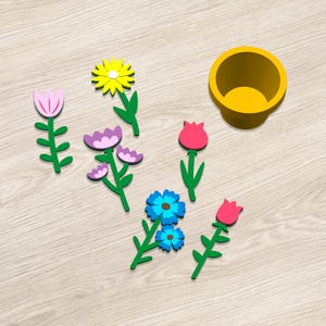 May include: A selection of brightly coloured wooden flower cutouts in pink, yellow, purple, and blue, plus a yellow flower pot. The flowers have green stems and are arranged on a light wood-grain surface.