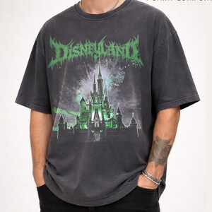 May include: Dark gray t-shirt with a distressed graphic featuring a castle and the word "DISNEYLAND" in green, gothic-style lettering. The shirt has a vintage, worn look and short sleeves. The text "PEPPER T-SHIRT COMFORT" is printed at the top.