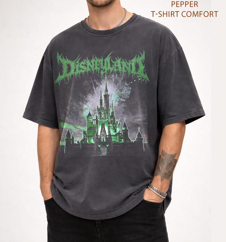 May include: Dark gray t-shirt with a distressed graphic featuring a castle and the word "DISNEYLAND" in green, gothic-style lettering. The shirt has a vintage, worn look and short sleeves. The text "PEPPER T-SHIRT COMFORT" is printed at the top.
