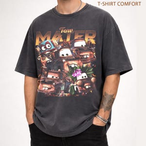 Puede incluir: Camiseta gris oscuro con un dise&ntilde;o del personaje Tow Mater de la pel&iacute;cula Cars. El dise&ntilde;o incluye el texto "Tow Mater" en una fuente desgastada, con im&aacute;genes del personaje. La camiseta est&aacute; etiquetada como "Pepper T-Shirt Comfort".