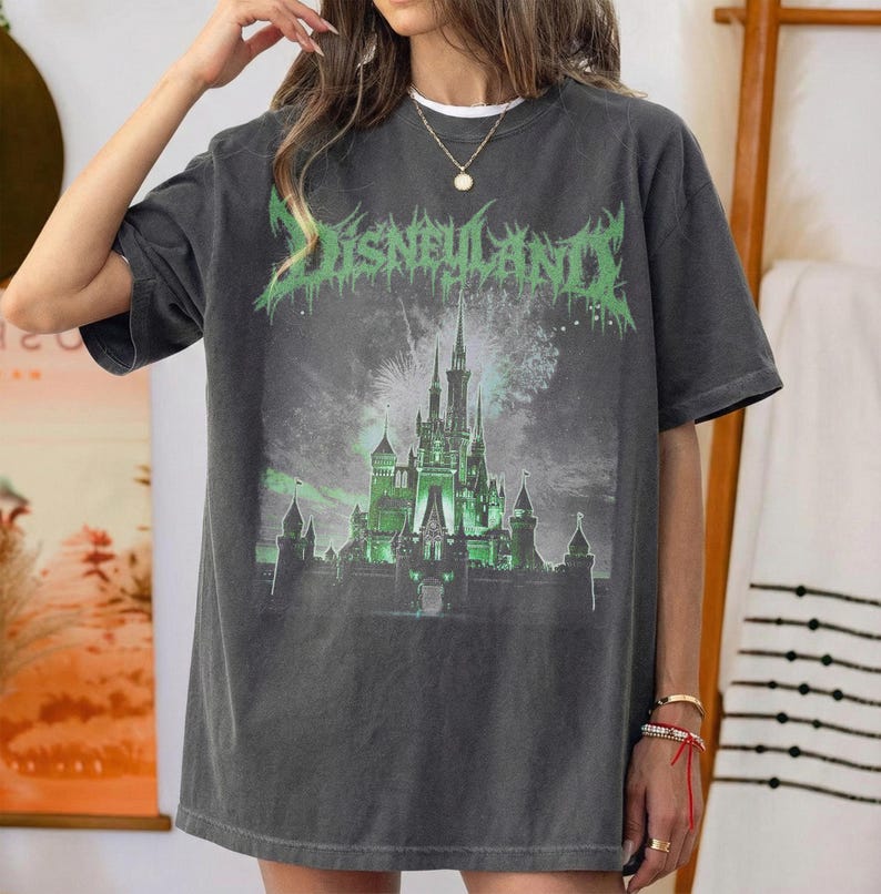 May include: Dark gray t-shirt featuring a green and white graphic of a castle with the text "DISNEYLAND" in a distressed font. The graphic tee has a vintage look and a relaxed fit.