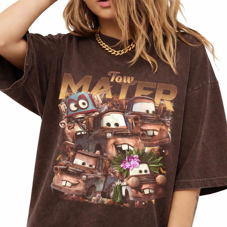 Puede incluir: Camiseta marr&oacute;n con un gr&aacute;fico del personaje Mater de la pel&iacute;cula Cars. El gr&aacute;fico incluye el texto "Tow Mater" en letras doradas. La camiseta tiene un aspecto vintage y desgastado.