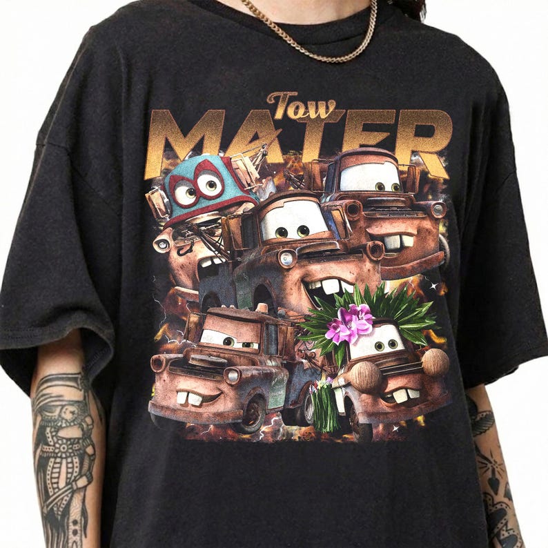 Puede incluir: Camiseta gris oscuro con un gr&aacute;fico del personaje Mater de la pel&iacute;cula Cars. La palabra "Tow" est&aacute; encima de la palabra "Mater" en letras doradas. El gr&aacute;fico incluye varias im&aacute;genes de Mater.