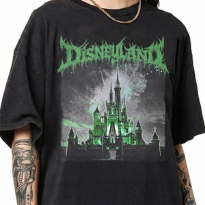 May include: Black t-shirt featuring a green and white graphic of a castle with the word "DISNEYLAND" in a stylized font. The castle is illuminated in green, with fireworks in the background.