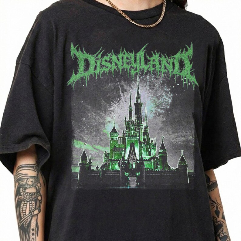 May include: Black t-shirt featuring a green and white graphic of a castle with the word "DISNEYLAND" in a stylized font. The castle is illuminated in green, with fireworks in the background.
