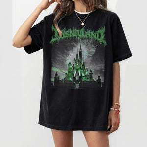 May include: Black t-shirt with a green graphic of a castle and the word "Disneyland" in a stylized font. The castle is illuminated in green, with fireworks in the background. The shirt has a relaxed fit.