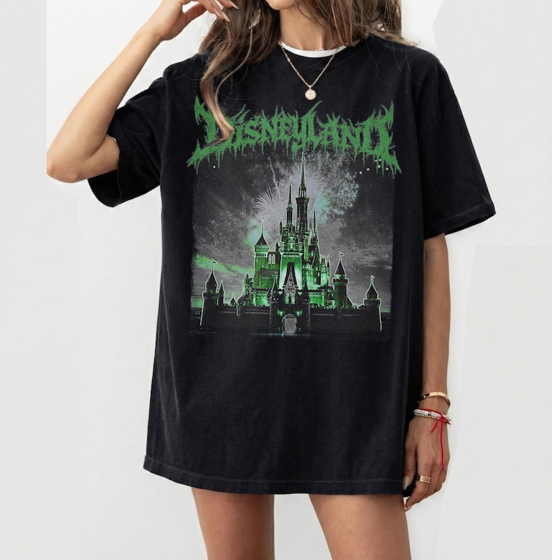 May include: Black t-shirt with a green graphic of a castle and the word "Disneyland" in a stylized font. The castle is illuminated in green, with fireworks in the background. The shirt has a relaxed fit.