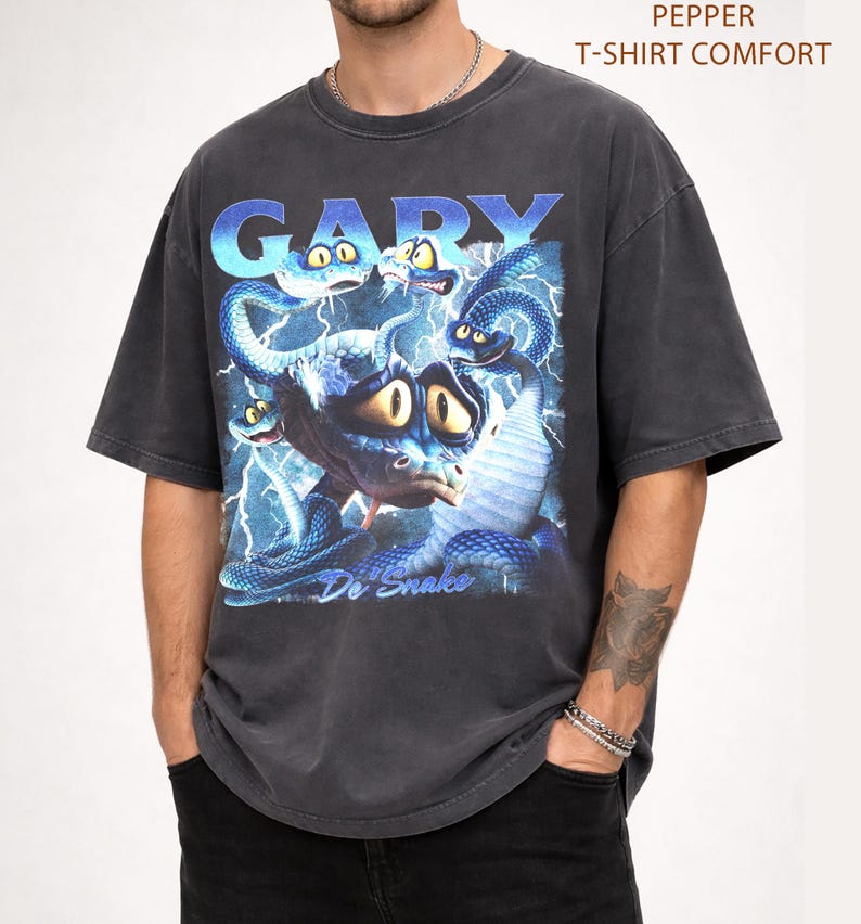 Pode incluir: T-shirt cinzenta escura com um gr&aacute;fico de uma criatura azul semelhante a uma cobra com olhos grandes e raios. A palavra "GARY" est&aacute; no topo em letras azuis, e o texto "Do Snake" est&aacute; na parte inferior. A camisa est&aacute; rotulada como "PEPPER T-SHIRT COMFORT".