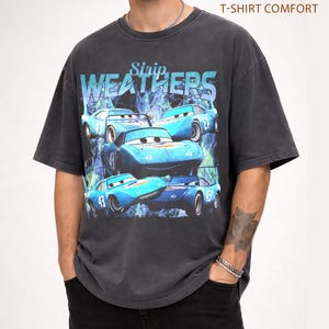 May include: Dark gray t-shirt featuring a graphic of blue race cars with the text "Strip Weathers". The cars have the number 43 on them. The shirt has a vintage, distressed look and the text "Pepper T-Shirt Comfort" is printed on the top right.
