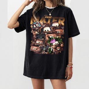 Puede incluir: Camiseta negra con un gr&aacute;fico del personaje Tow Mater de la pel&iacute;cula Cars. El dise&ntilde;o incluye m&uacute;ltiples im&aacute;genes de Mater con la palabra "Tow Mater" en letras doradas encima de las im&aacute;genes del personaje.