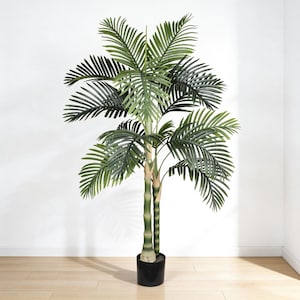 May include: A tall artificial palm tree with multiple green fronds and a bamboo-like trunk. The tree is potted in a black plastic pot and stands on a light-colored wooden floor. The background is a plain white wall.