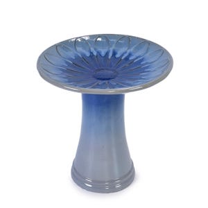 May include: A ceramic bird bath with a blue and gray ombre design. The bowl has a flower-like pattern with a gray rim. The pedestal base is a matching blue and gray gradient. A decorative garden accent.