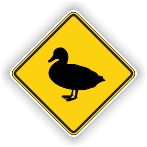Könnte beinhalten: Ein gelbes, rautenförmiges Warnschild mit einer schwarzen Silhouette einer Ente. Das Schild dient dazu, Autofahrer vor Enten zu warnen, die die Straße überqueren.