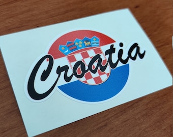 Può includere: Un adesivo con lo stemma croato e la parola "Croatia" in un carattere nero. Il design include uno scudo a scacchi rosso e bianco, un cerchio blu e uno sfondo a strisce rosse e bianche.