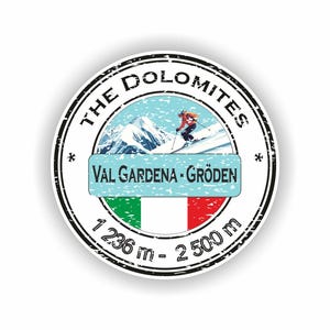 May include: A round sticker with a black border featuring the text "THE DOLOMITES" and "VAL GARDENA - GRÖDEN". The sticker includes an illustration of a skier, mountains, and the Italian flag. The sticker also displays the altitude range of 1236 m - 2500 m.