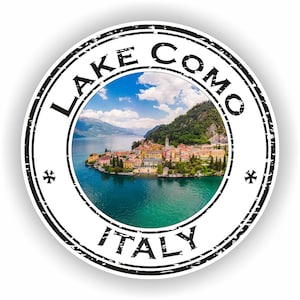 May include: A vintage-style round stamp with the text "LAKE COMO ITALY" in black lettering. The stamp features a photo of a small town on a lake with mountains in the background.