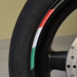 Può includere: Un pneumatico nero per moto con un design a strisce bianche, verdi e rosse. Il pneumatico ha la scritta "TREAD", "SIDEWALL PLIES RAYON" e "SPLIES RAYON" stampata su di esso.