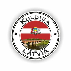 Könnte beinhalten: Ein runder Aufkleber mit der lettischen Flagge, bestehend aus roten und weißen Streifen und einem Wappen. Die Worte "Kuldiga Latvia" sind in einer verwitterten schwarzen Schrift um die Flagge gedruckt. Am unteren Rand des Bildes ist eine Brücke zu sehen.