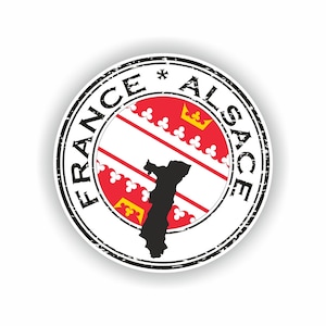 May include: A black and white circular stamp with the text "FRANCE*ALSACE" around the edge. The center of the stamp features the flag of Alsace, a red and white striped flag with yellow fleurs-de-lis and crowns. A black silhouette of the Alsace region is superimposed on the flag.