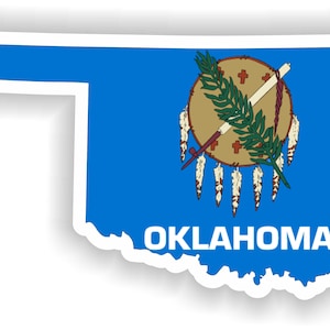 May include: A blue sticker with the outline of the state of Oklahoma. The state seal is in the center of the sticker, which features a shield with a crossed spear and arrow, a green branch, and five white feathers. The word "OKLAHOMA" is printed in white below the seal.