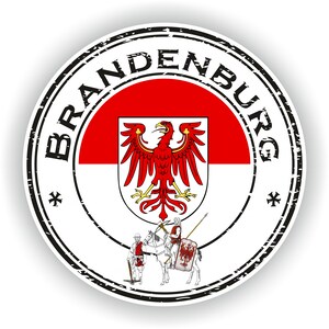 Può includere: Un francobollo circolare in bianco e nero con la parola "BRANDENBURG" attorno al bordo. Il centro del francobollo presenta lo stemma di Brandeburgo, che include un'aquila rossa con uno scudo bianco e una bandiera rossa e bianca.