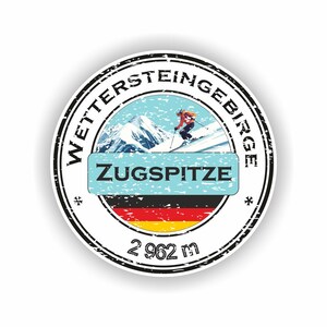 Könnte beinhalten: Runder Aufkleber mit schwarzem Rand. Er zeigt den Text "WETTERSTEINGEBIRGE" und "ZUGSPITZE". Das Design umfasst einen Skifahrer, Berge und die deutsche Flagge. Der Aufkleber zeigt auch "2 962 m".