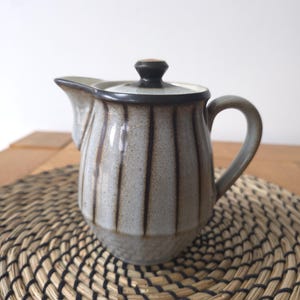 Peut inclure: Un pot à lait en céramique avec un émail gris clair moucheté et des rayures verticales brun foncé. Le pot présente une anse incurvée, un bec verseur pointu et un couvercle assorti avec un petit bouton sur le dessus, finition texturée.