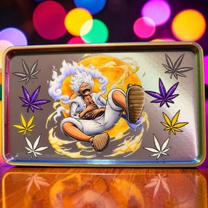 May include: Rectangular metal rolling tray with a cartoon illustration of a character with white hair and a yellow background. The tray has a gold border and features cannabis leaf designs in various colors.