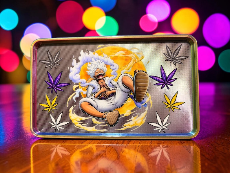 May include: Rectangular metal rolling tray with a cartoon illustration of a character with white hair and a yellow background. The tray has a gold border and features cannabis leaf designs in various colors.