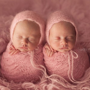 Puede incluir: Dos bebés recién nacidos con gorros de punto rosa y envueltos en mantas rosas. Los bebés duermen plácidamente.