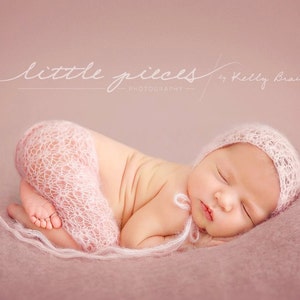 May include: A newborn baby sleeping peacefully on a pink blanket, wearing a white crocheted hat and a matching wrap. The baby is curled up in a fetal position with their eyes closed.