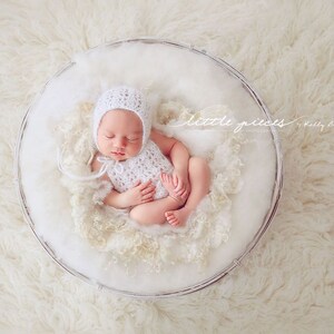 May include: A newborn baby wearing a white crocheted hat and dress is sleeping in a white basket. The basket is filled with white fluffy material. The image is captioned "little pieces photography by Kelly Brown".