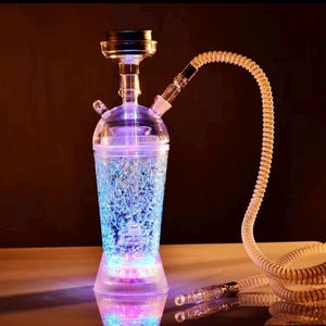 May include: A clear, illuminated hookah with a cylindrical base and a bulbous top. The base and top emit a colorful glow, with blue and purple hues. A flexible, cream-colored hose extends from the top.