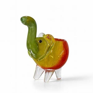 Può includere: Una colorata statuetta a forma di elefante in vetro con una proboscide e una testa verdi, che sfumano in giallo e rosso sul corpo. L'elefante ha zampe di vetro trasparente e una piccola apertura sul dorso. Un oggetto decorativo unico.