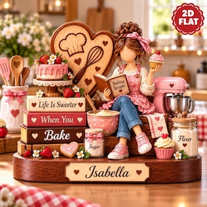 May include: A decorative figurine of a person holding a cupcake and a book titled Baking Recipes, sitting on a stack of books labeled Life Is Sweeter When You Bake. Includes a heart-shaped board, a pink mixer, and jars labeled Sugar and Flour.