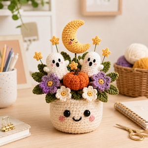 May include: A crocheted arrangement in a cream-colored pot with a smiling face. It features two white ghosts, an orange pumpkin, a yellow crescent moon with a sleepy face, purple and white flowers, green leaves, and small yellow stars on stems.