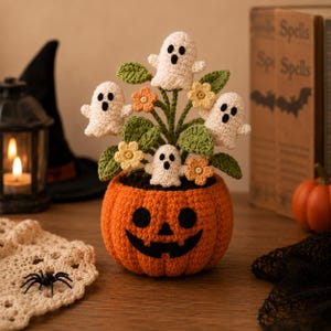 May include: A crocheted orange jack-o'-lantern pot containing a bouquet of green leaves, small yellow flowers, and four white ghosts with black eyes and mouths. The ghosts are positioned among the foliage, creating a decorative arrangement.