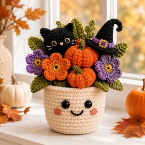 May include: A crocheted arrangement in a cream-coloured pot with a smiling face, featuring a black cat, two orange pumpkins, a black witch hat with a purple band, and purple and orange flowers with green leaves, all crafted from yarn.